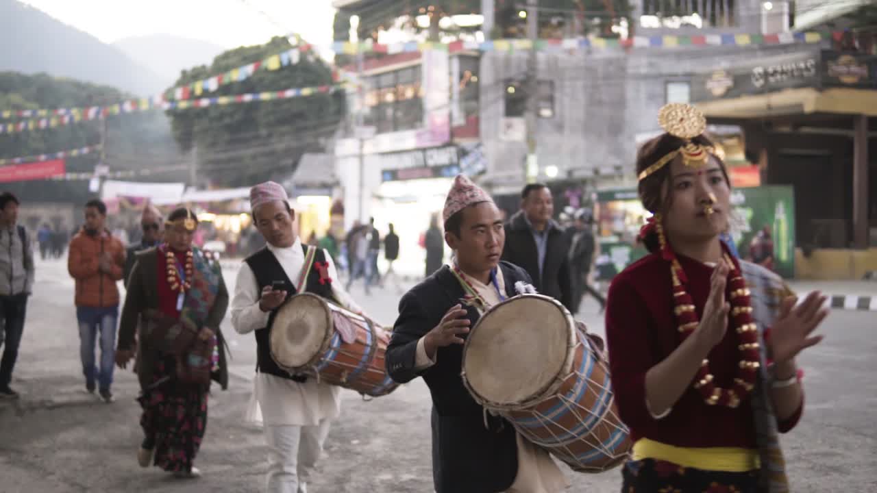 Nepali people wearing traditional dress carrying traditional music instruments walking alongside the road with the crew.