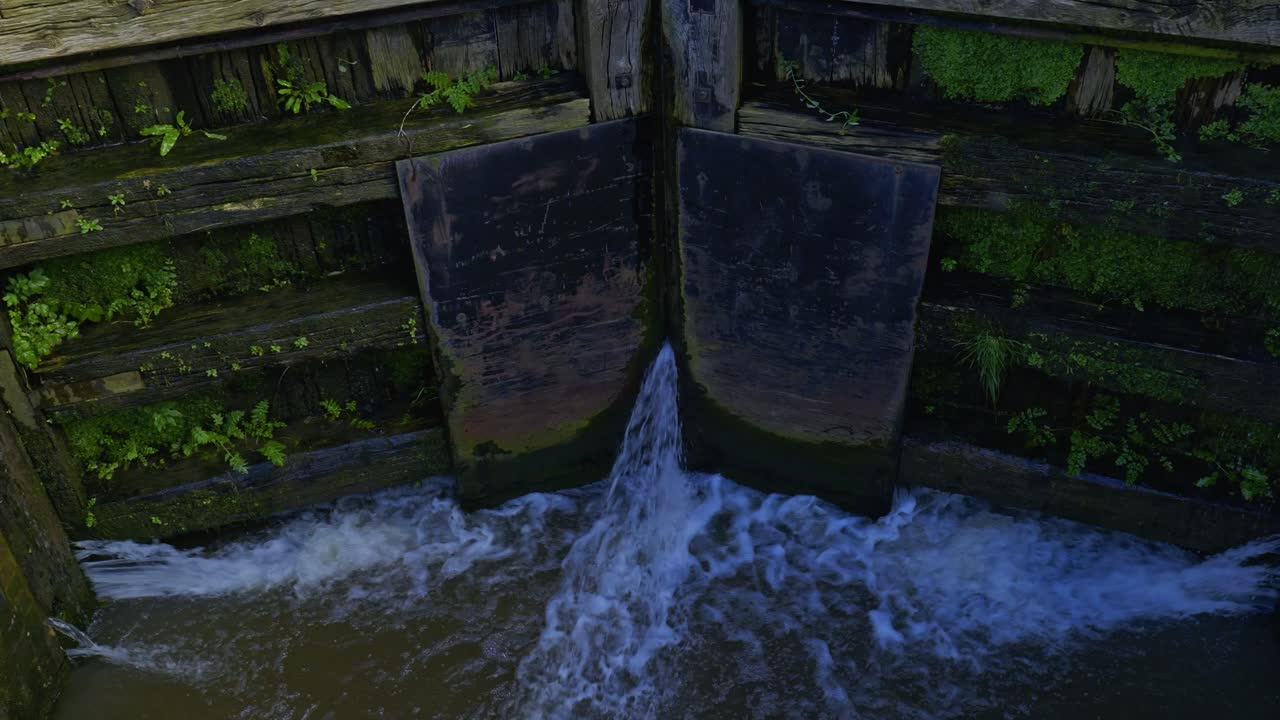 Canal lock with water pouring throuigh large wooden gates into old barge narrowboat lift system