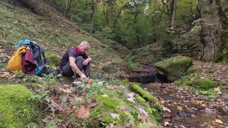 young caucasian male hiker brews tea by autumn forest babbling brook