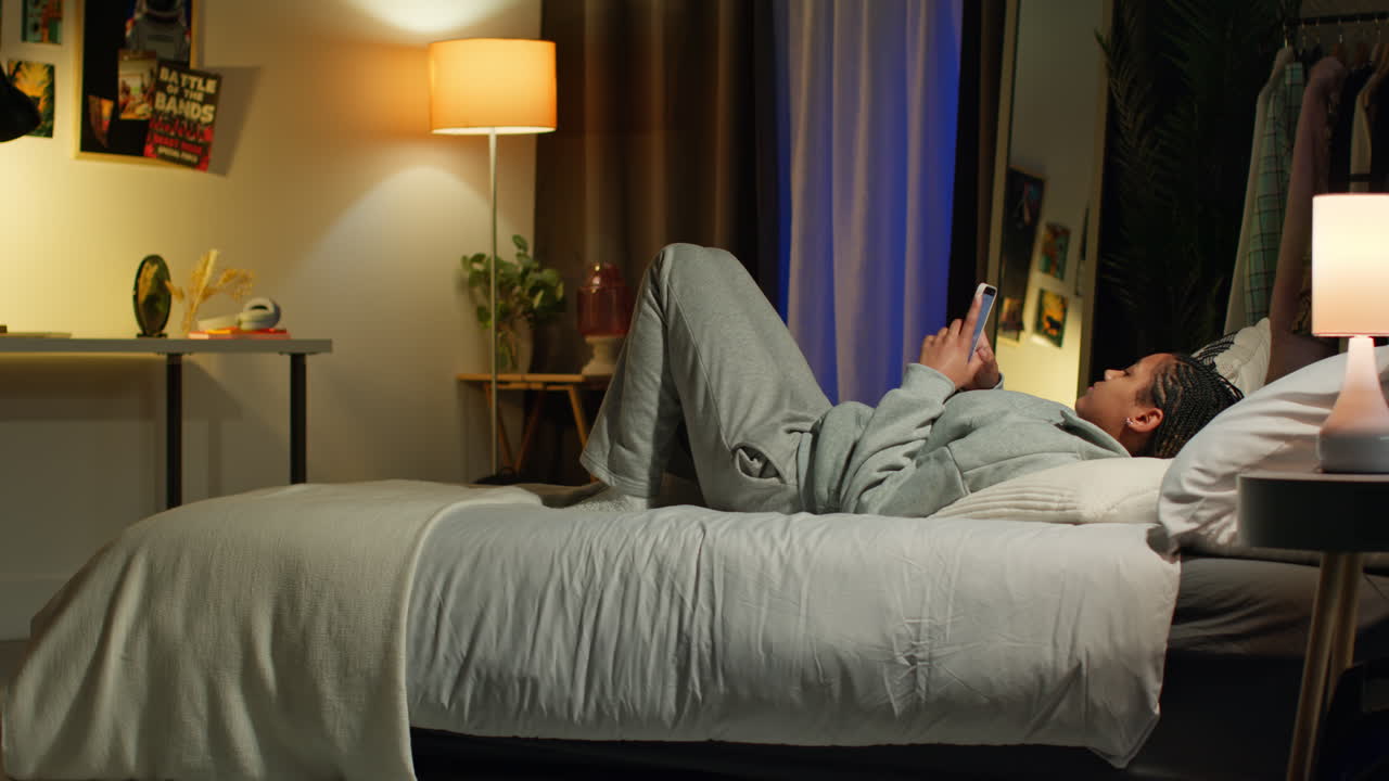 십대가 밤에 침실에서 스마트폰을 사용하고 있습니다.