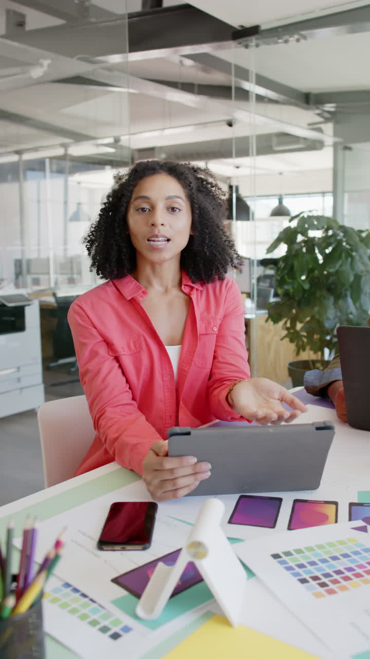Vertical video of portrait of happy biracial businesswoman with tablet having video call