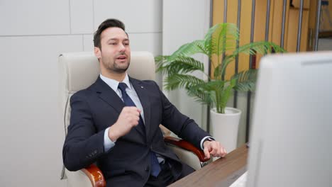 satisfied businessman finished work on computer while sitting at desk at workplace in business office. cheerful young corporate man doing an excited fist pump and celebrating his success or victory
