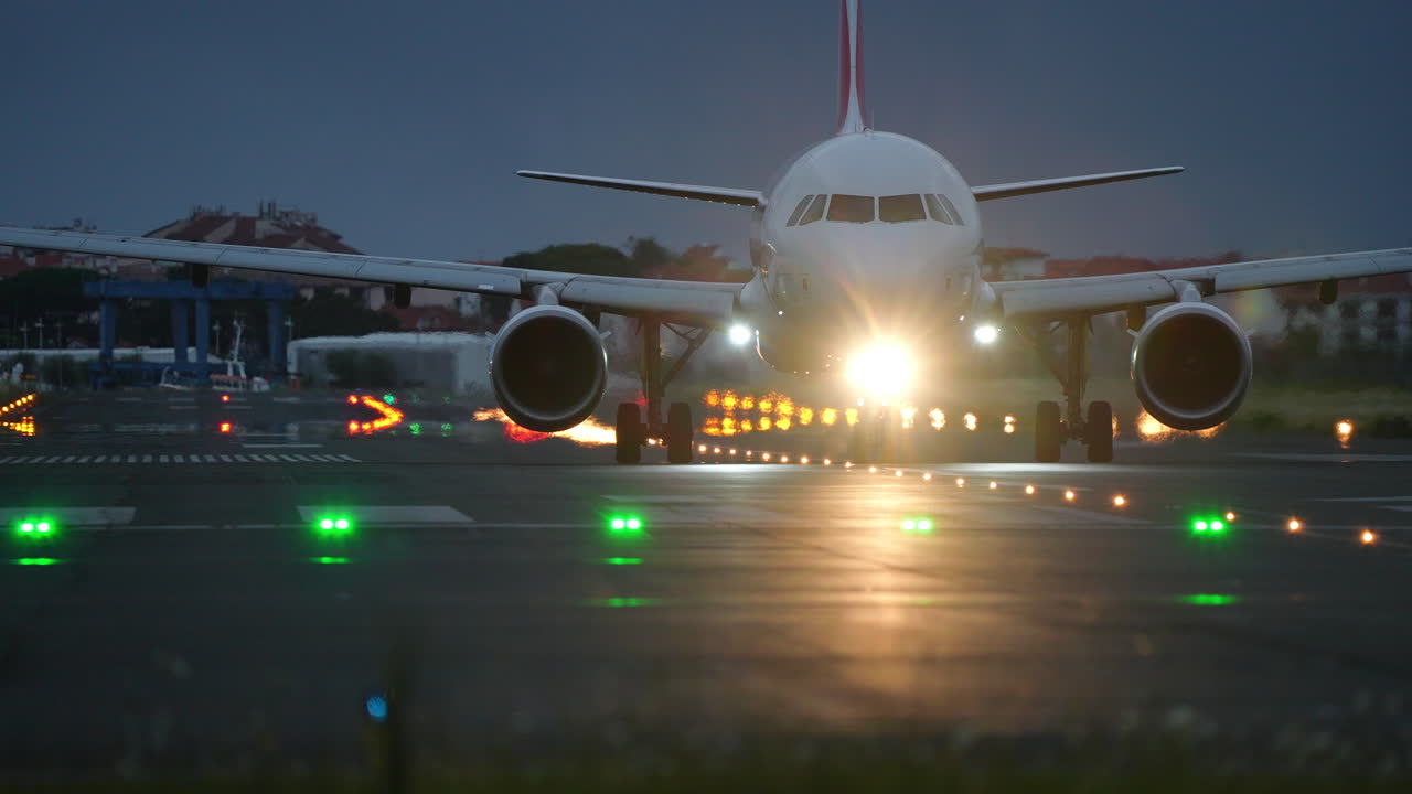 Airplane is taxiing on runway at night, surrounded by illuminated lights and a dark sky, creating a dramatic aviation scene