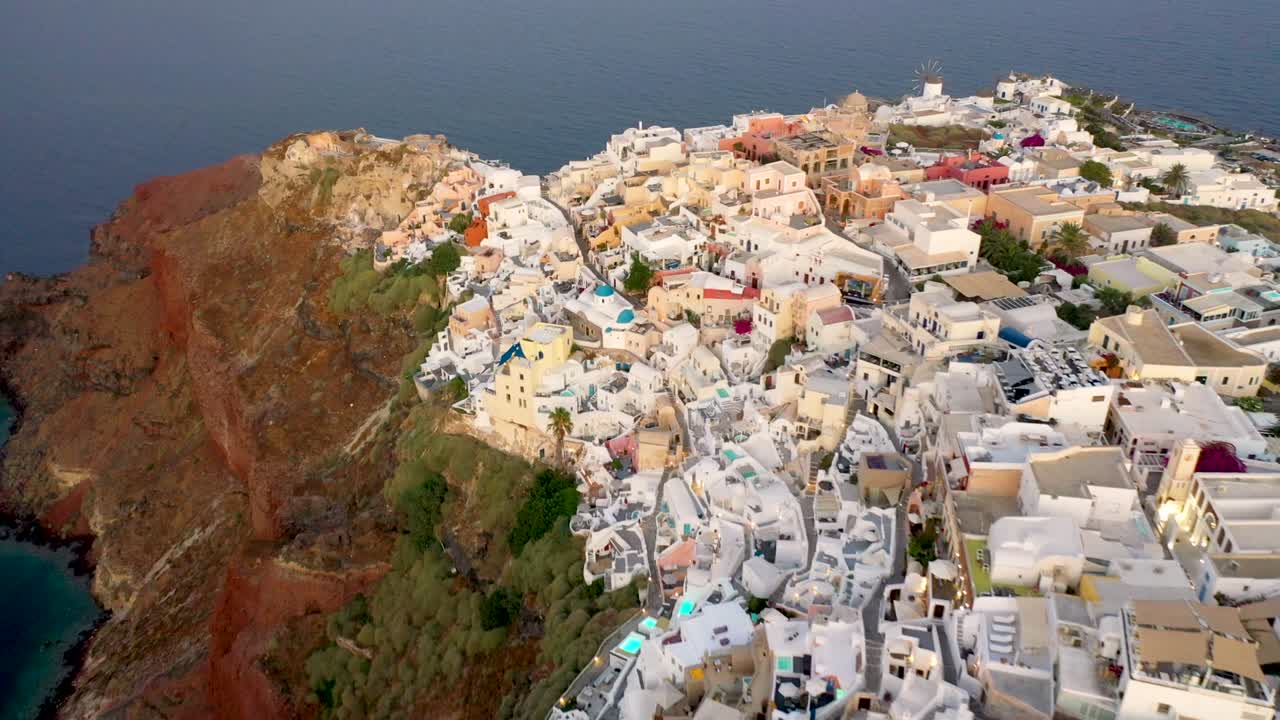 video de drones del famoso pueblo pintoresco blanco y colorido de oia construido sobre un acantilado al atardecer, isla de santorini, cícladas, grecia