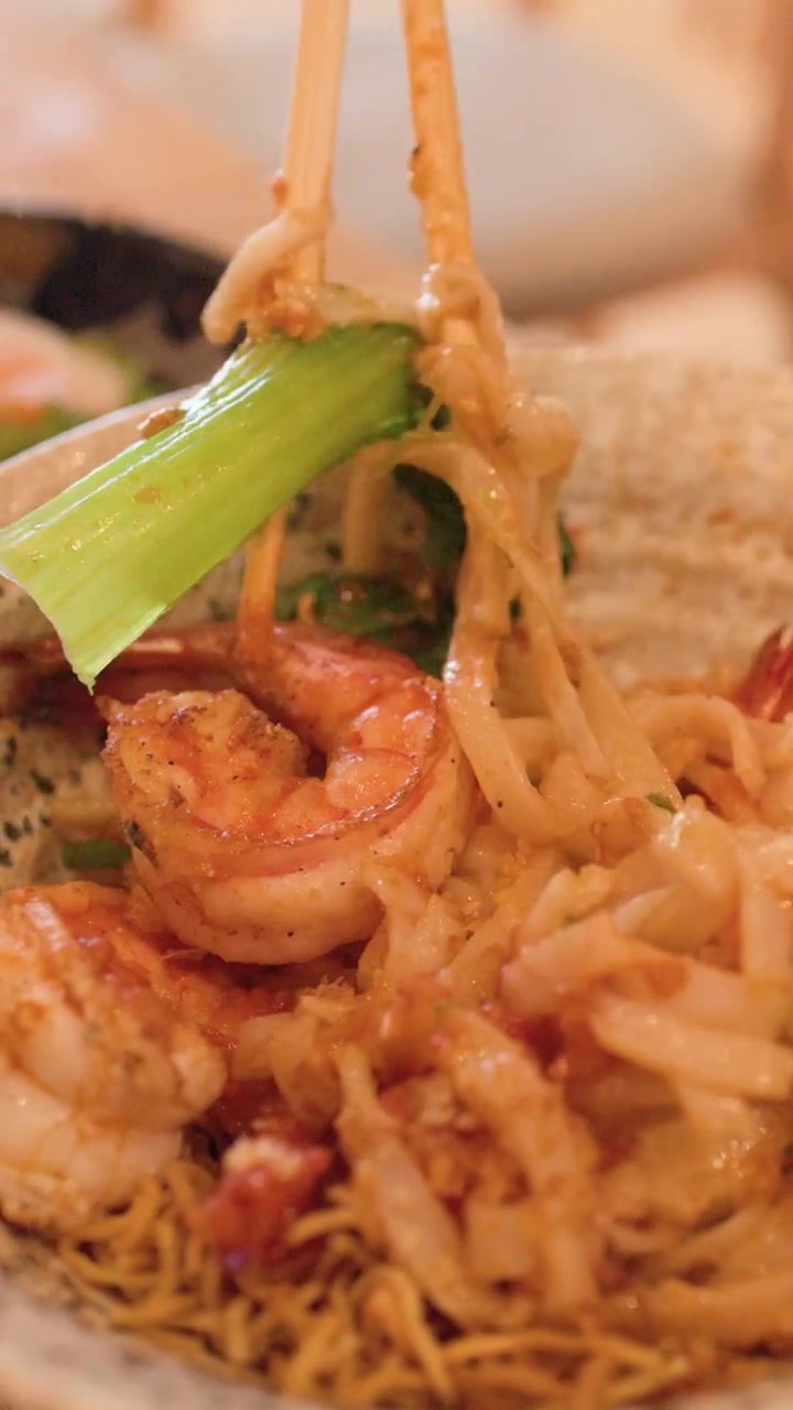 Primo piano di una persona che solleva noodles Shan birmani e gamberi con le bacchette a Bangkok, Thailandia.