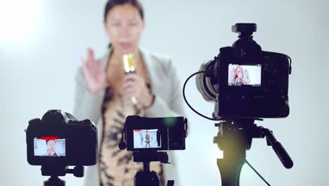 a female television show host does a sound check with a microphone - focus on cameras in the foreground