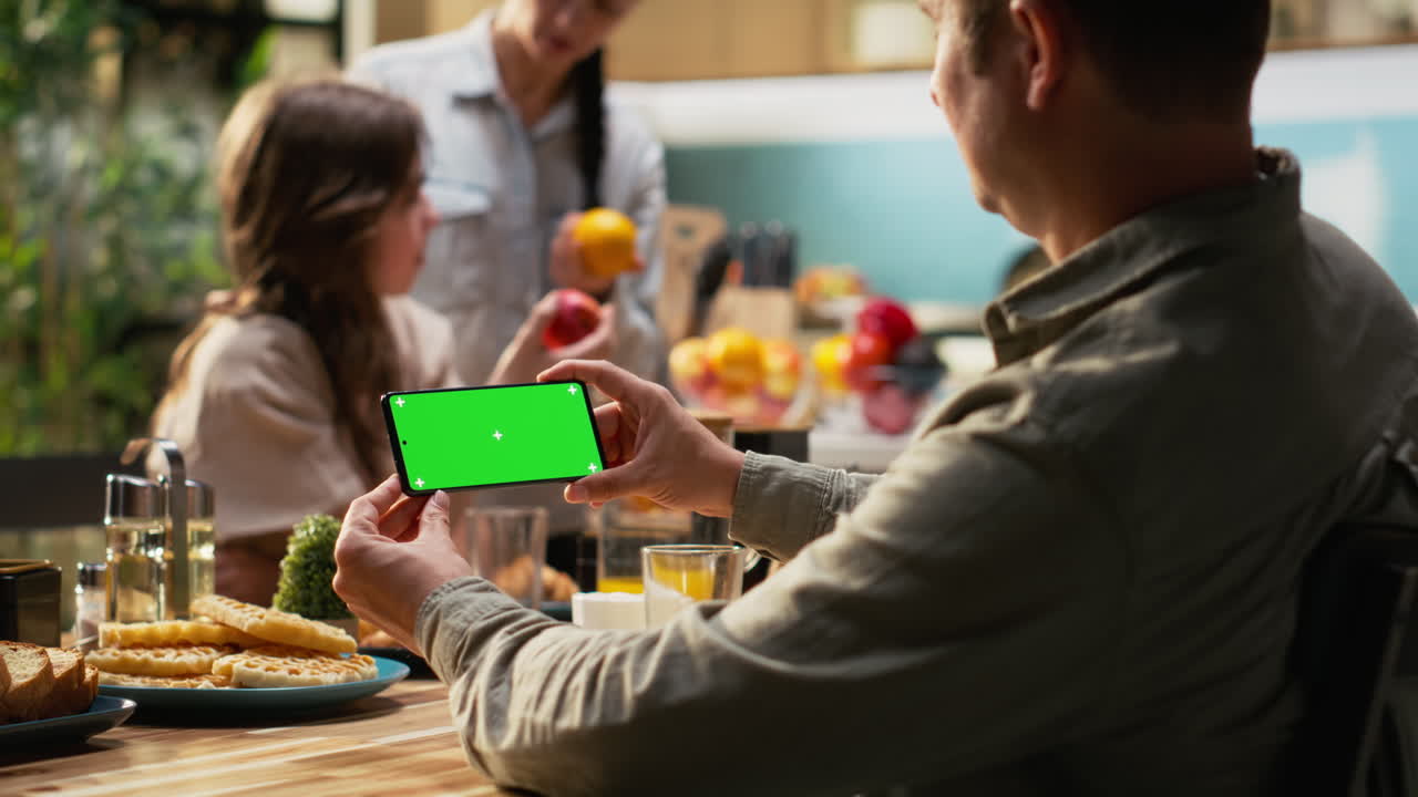 Green screen on smartphone with family serving breakfast at home