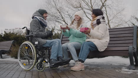 happy disabled man in wheelchair celebrating his birthday with two friends at urban park in winter