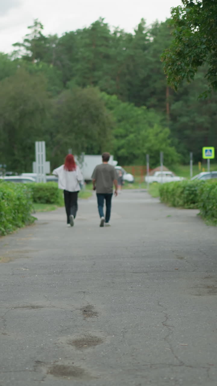회색 을 입은 어린 소년은 자전거를 타고 포장된 길을 돌아다니며, 두 사람이 멀리서 걸어가고, 배경에는 푸른 초록색으로 둘러싸인 차의 흐릿한 시야가 있습니다.