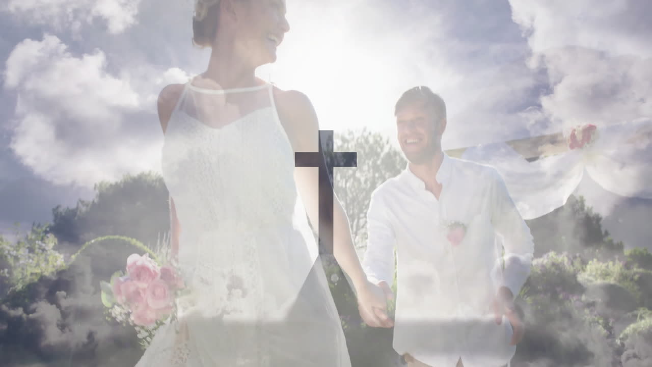 Holding hands under bright cloudy sky, couple in wedding attire smiling