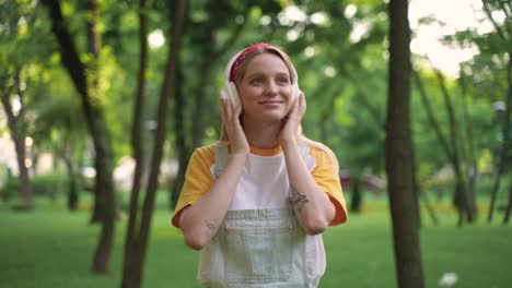 hermosa joven escuchando música con auriculares y smartphone mientras camina en un parque verde