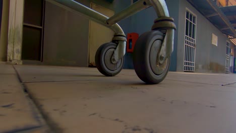 Grocery-shopping-cart-wheels-under-carriage-metal-in-extreme-slow-motion-on-tile-out-doors-at-dusk-close-up