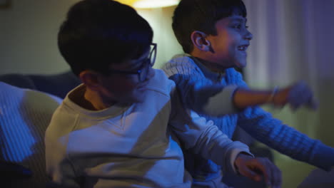 two young boys at home having fun playing with computer games console on tv fighting over controllers late at night