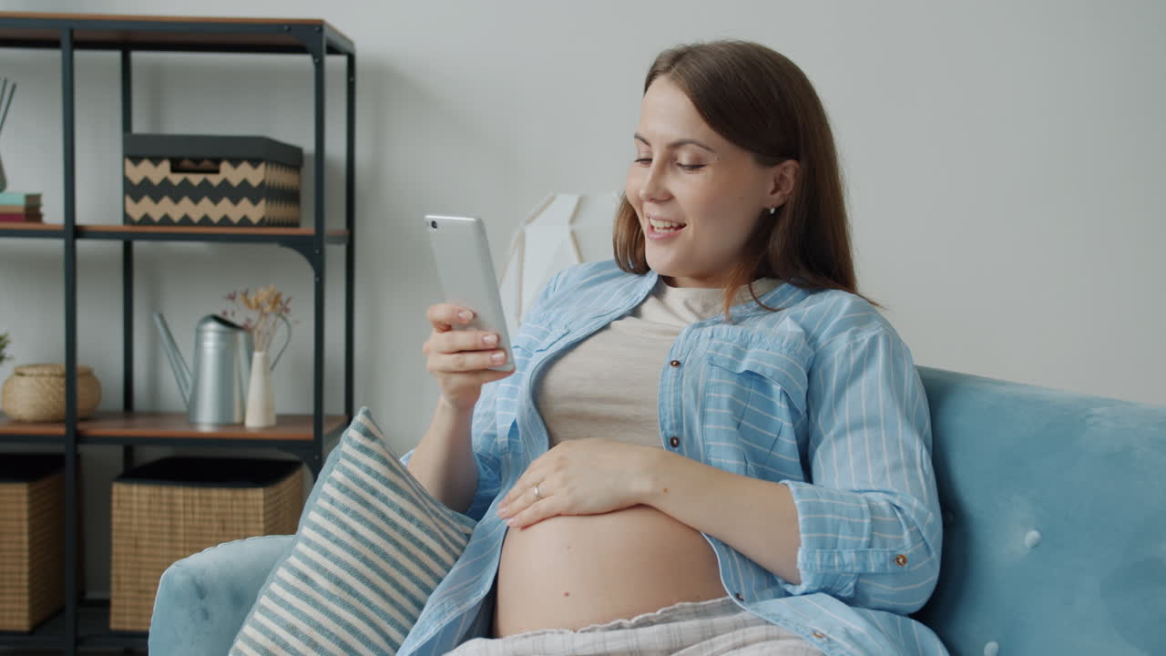 Pregnant woman looking at phone on sofa