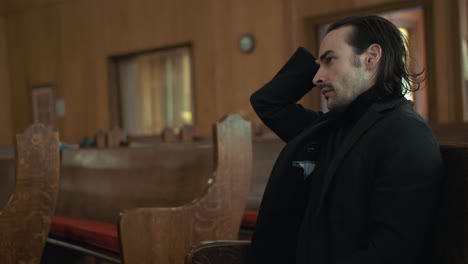 estresado, ansioso, emocional, hombre sombrío en traje negro sentado en el banco de la iglesia en cámara lenta cinematográfica