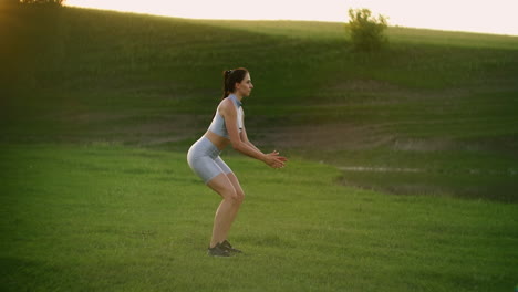 una chica joven en un parque al atardecer se para en una pierna y salta.