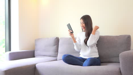 휴대전화를 손에 들고 모바일 게임을 하는 30대 아시아 여성, 게임에서 이겼을 때 흥분한 표정