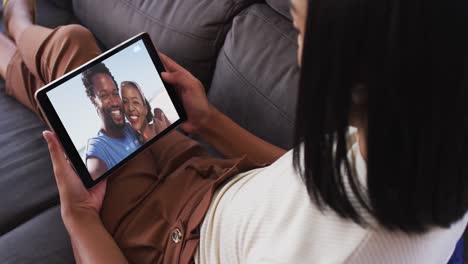 Mujer-Afroamericana-Haciendo-Una-Videollamada-En-Una-Tableta-Digital-Sentada-En-El-Sofá-De-Casa