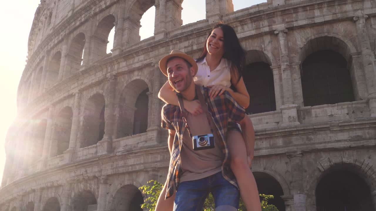 Ungt turistpar danser, snurrer rundt og holder hender ved Colosseum ved soloppgang. Roma, Italia.