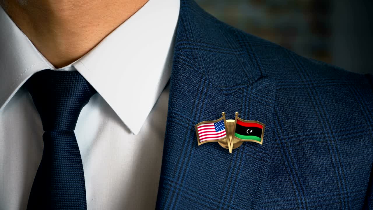 hombre de negocios caminando hacia la cámara con banderas de países amigos pin estados unidos de américa - libya.mov