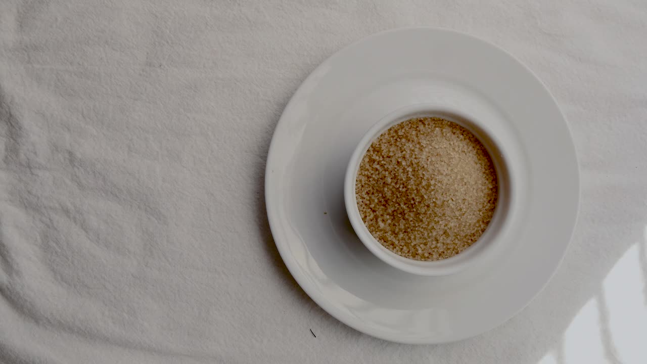 흰색 매트에 있는 흰색 세라믹 식기에 있는 생 갈색 설탕