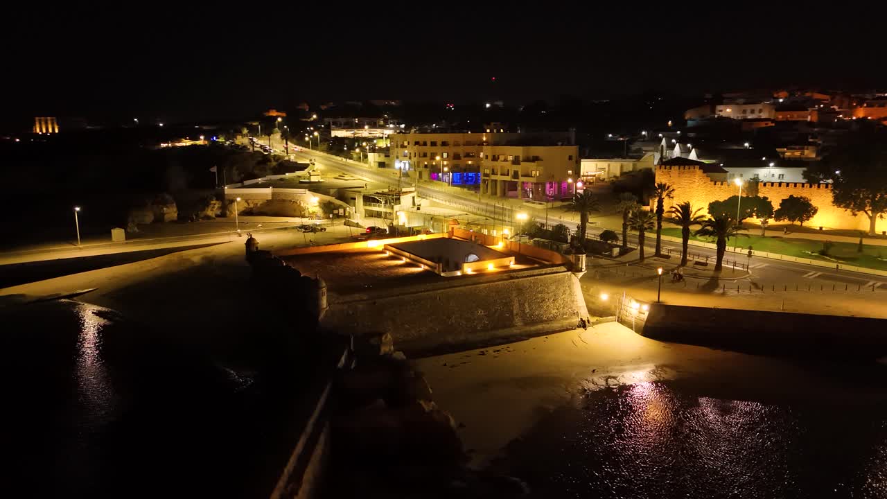 Aerial view of Ponta da Bandeira Fort illuminating the Algarve coast at night in Lagos, Portugal. Orbit Motion