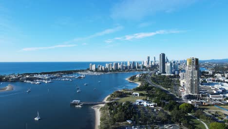 High-revealing-aerial-view-of-a-coastal-urban-metropolitan-sprawl-with-a-towering-high-rise-skyline-and-city-parkland-below