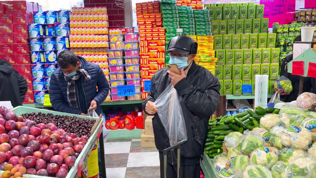 Nueva York, EE. UU., 9 de marzo de 2022: Compradores junto a exhibiciones de ciruelas y pepinos en el mercado. Compradores con mascarilla de pie cerca de exhibiciones de ciruelas y pepinos con estantes de productos envasados detrás.