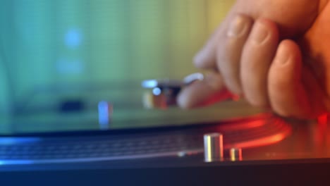Defocus in focus. Vinyl player turntable. A fragment of a rotating vinyl plate, a stylus with needles close-up. The girl's hand removes the stylus from the plate. Blurred against the background of red
