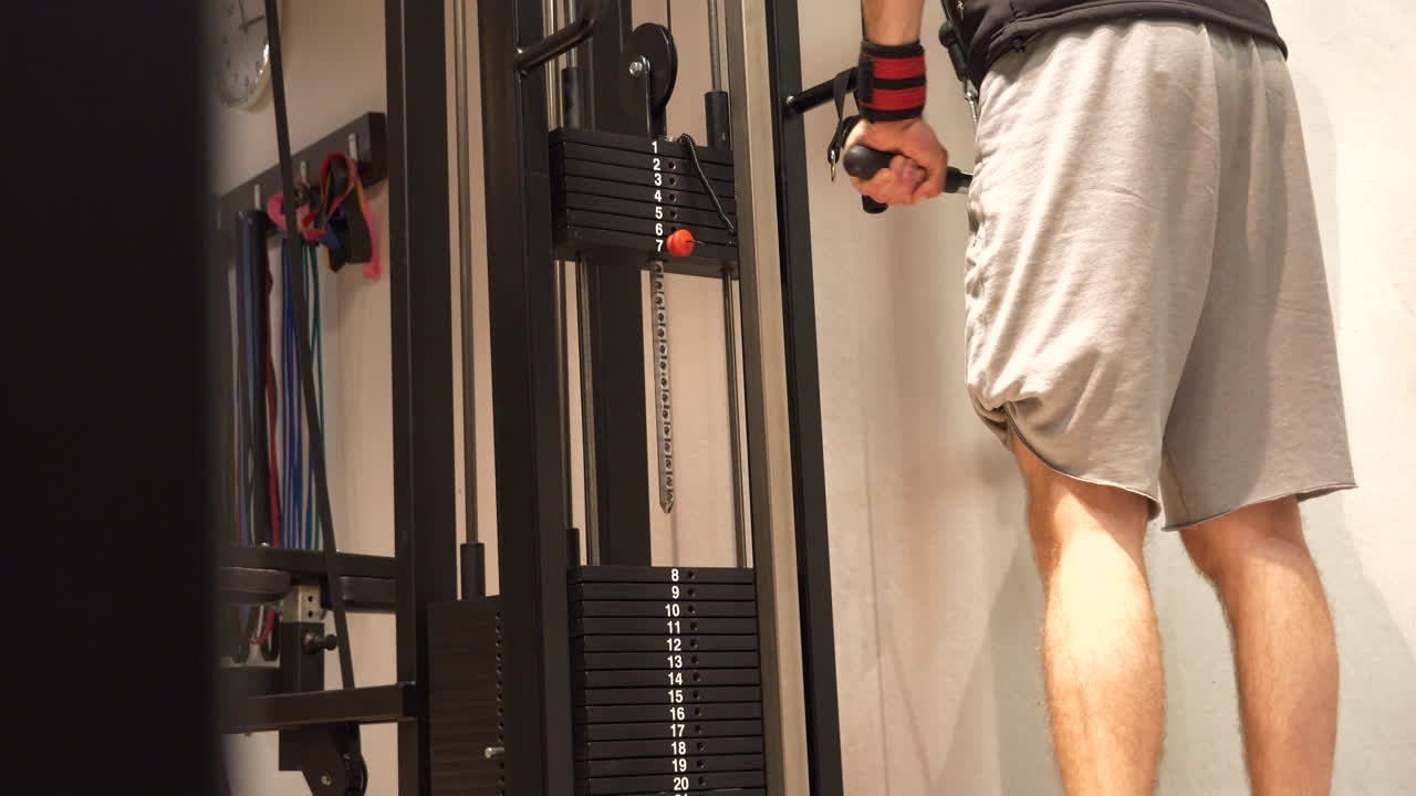 vista de ángulo bajo, detrás del hombre que usa la máquina de pesas para los músculos del brazo, tiro estático