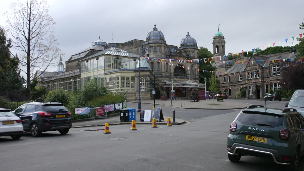 The Buxton Opera House in England, with its elegant domed towers and glass conservatory visible. Colorful bunting decorates the area, adding a festive touch to the historic setting