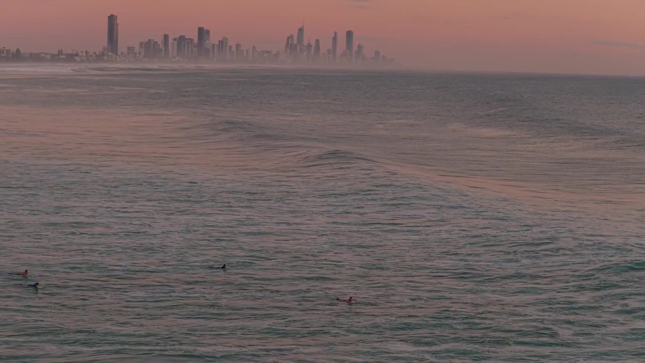 Surfisti sull'oceano mosso con lo skyline di Surfers Paradise sullo sfondo all'alba nebbiosa in Australia. - ripresa aerea