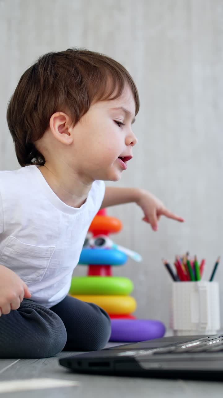 Un adorabile bambino piccolo preme un tasto sul laptop e batte le mani allegramente. Il bambino indica lo schermo e chiude il dispositivo. Ripresa dal basso. Video verticale.