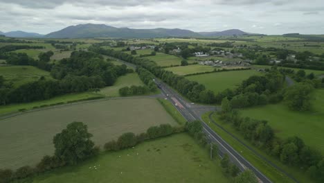 Busy-rural-road-A66-with-mountain-Blencathra-in-the-distance-and-green-patchwork-fields-on-overcast-summer-day