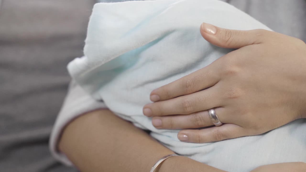 primer plano de las manos de una joven madre acariciando mientras lleva a un bebé envuelto en una toalla blanca