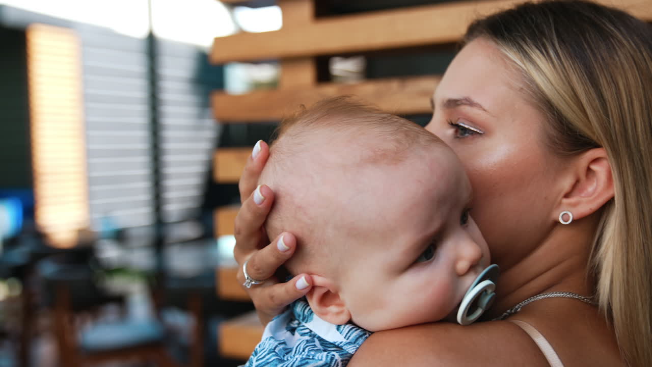 Blonde woman is holding her baby boy. Mother is calming her infant with pacifier in mouth. Close up.