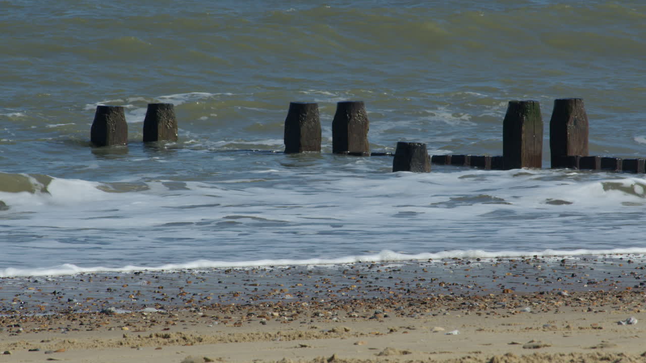 Mid shot of the waves crashing over the sea defence groynes at Walcott Beach