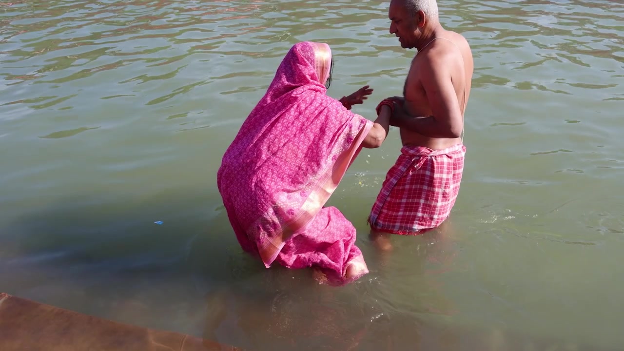 Pareja de ancianos devotos ayudándose mutuamente para un baño sagrado en un río sagrado durante una peregrinación religiosa.