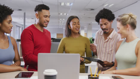 Happy-diverse-male-and-female-business-colleagues-talking-and-using-laptop-in-office