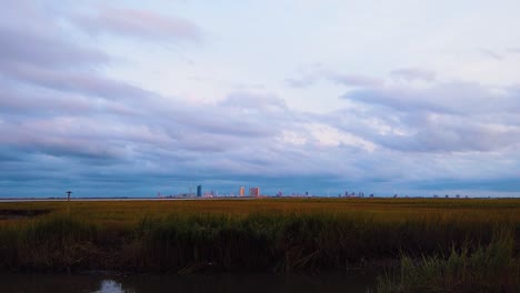 hd motionlapse acerca y mantiene el horizonte de la ciudad atlántica a distancia sobre un canal con un cielo mayormente nublado de día a noche con nubes que se vuelven rosadas, moradas y azules