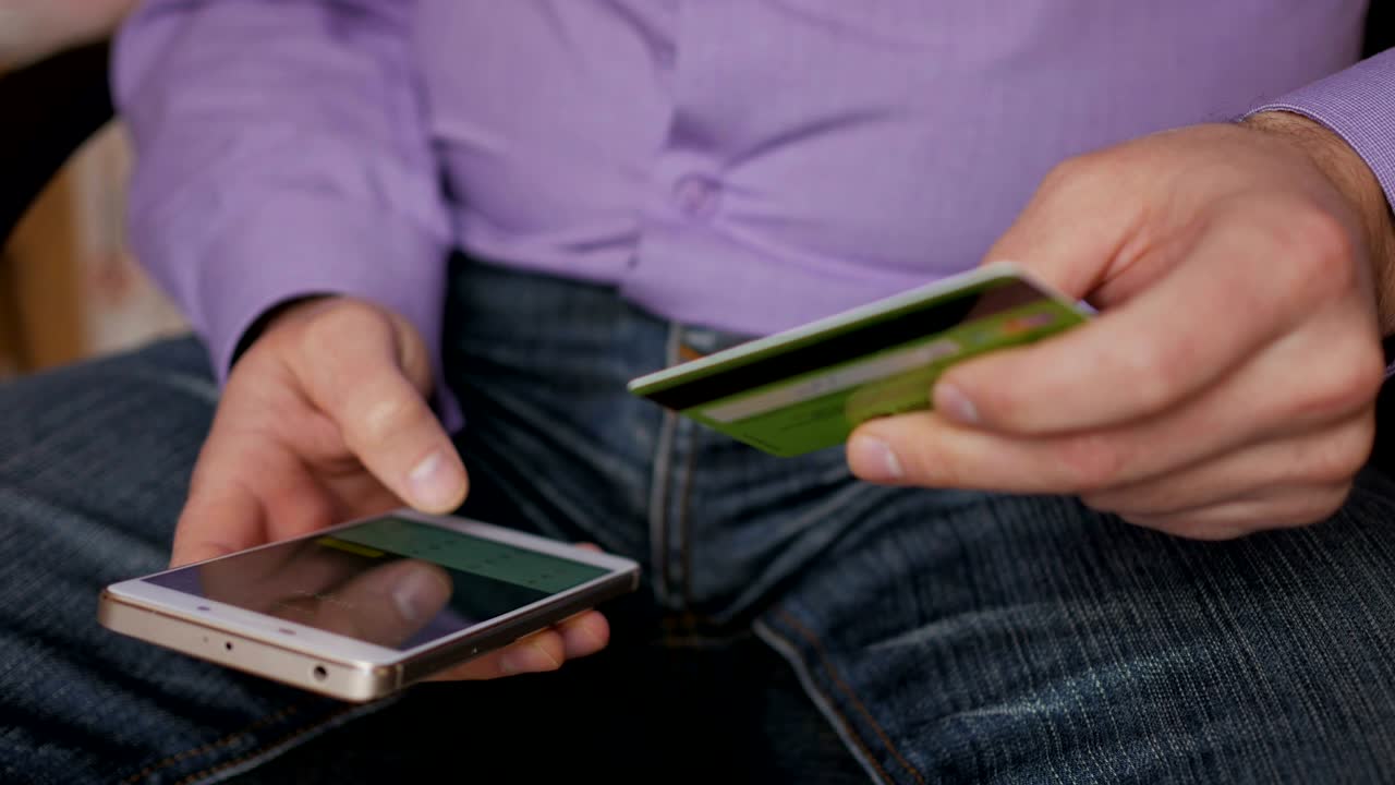 hombre de negocios con una camisa púrpura haciendo pago en línea con tarjeta de crédito y teléfono inteligente, compras en línea, tecnología de estilo de vida. hombre introduce el número de tarjeta bancaria en el teléfono inteligente. primer plano. primer plano