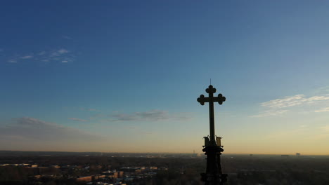 an aerial shot of a cathedral's steeple with a cross on it during at sunrise