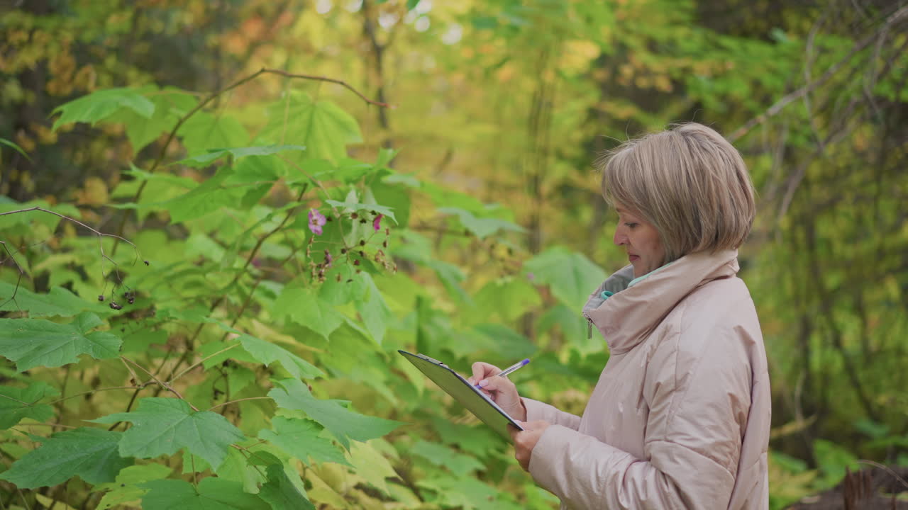 female scientist examining blooming plant closely while documenting observations with clipboard in hand, surrounded by vibrant green foliage and soft yellow autumn hues in quiet forest