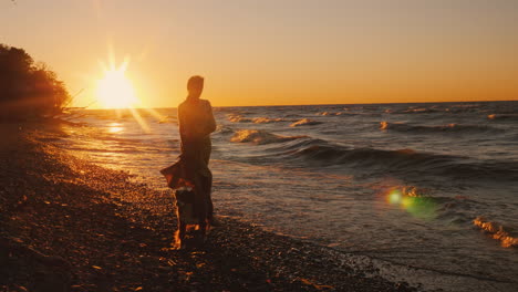 Eine-Junge-Frau-Geht-Mit-Einem-Hund-Am-Ufer-Des-Sees-Ontario-Bei-Sonnenuntergang-Windiges-Wetter-Schöner-Sonnenuntergang