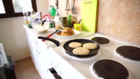 three pancakes are fried in a frying pan, on an electric stove, against the background of the kitchen table.