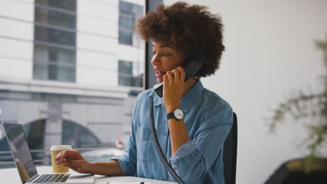 Mujer-De-Negocios-En-Una-Oficina-Moderna-Trabajando-En-Una-Computadora-Portátil-Y-Hablando-Por-Teléfono-De-Escritorio