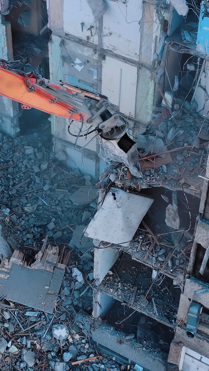 Excavator crashing floors of an old building and dusty debris falling down. Disassembling of collapsed structures. View from above. Vertical video