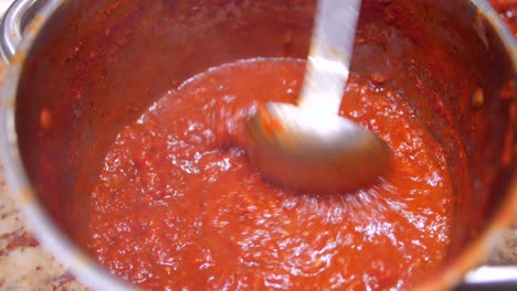 close up view of homemede tomato sauce boiling in a pan, being stirred with a spoon