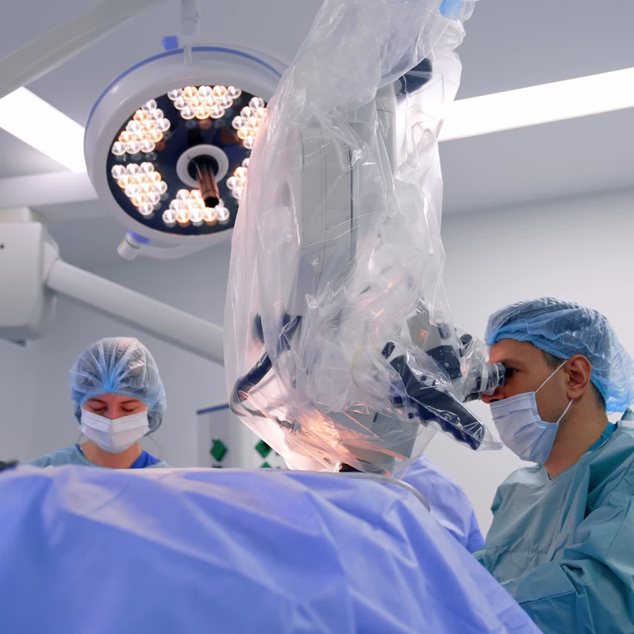 Neurocirujano operando a un paciente con un microscopio tecnológico. Dos asistentes médicos al fondo.