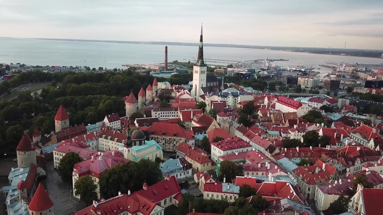 Impresionantes imágenes de dron del casco antiguo medieval de Tallin al atardecer. La toma muestra la colina de Toompea, la Catedral de Santa María y edificios con tejados rojos bajo un cielo dramático de nubes rosas y naranjas.